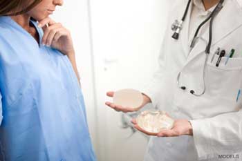 Doctor holding two breast implants out to woman