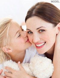 Woman smiling while little girl kisses her on the cheek