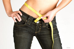 Woman's bare abdomen with tape measure around the waist wearing dark blue jeans