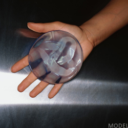 Hand holding out a breast implant in an open palm