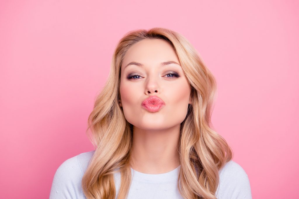 Woman shows off her full lips with a pursed, air kiss.