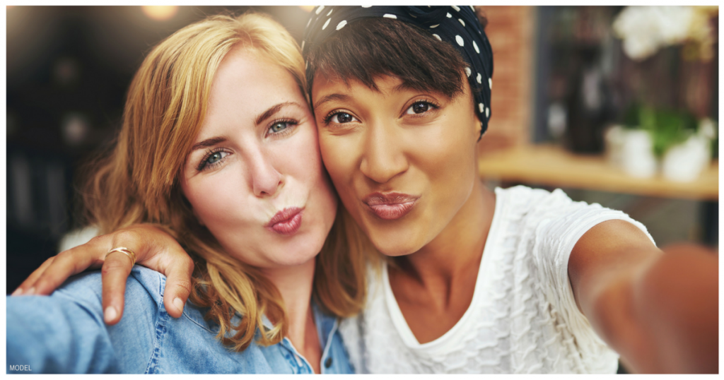 Two women with arms around each other and lips puckered taking a selfie