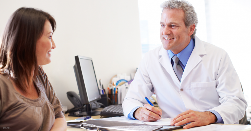 Doctor in white lab coat sitting at a desk and talking with a woman.