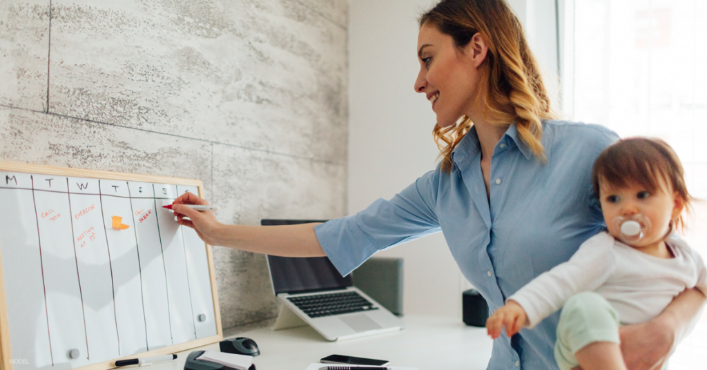 Woman holding a baby on her hip while writing on a white board