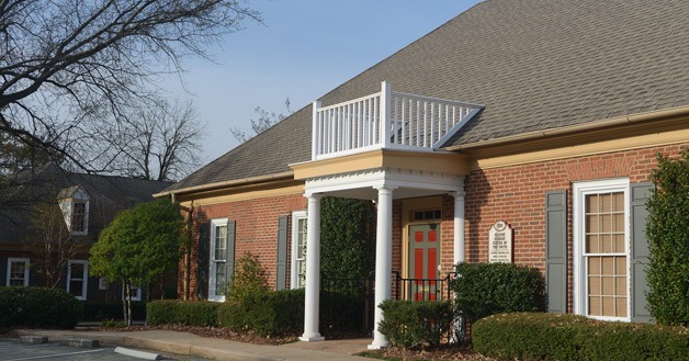Single story red brick building with white columns framing the doorway
