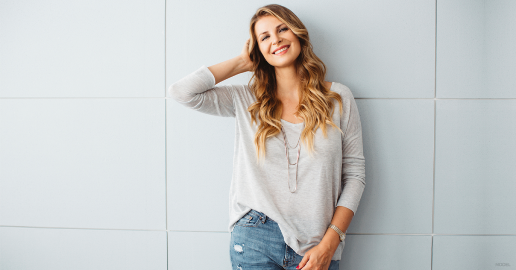 Young woman with long, light brown hair leaning against a wall and smiling