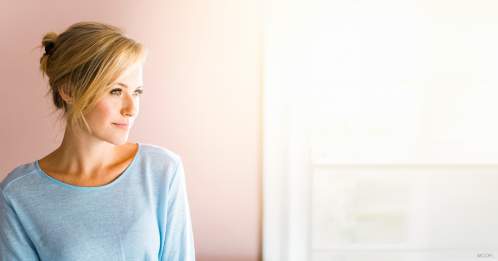 Woman looking out window considering breast augmentation in Marietta, Georgia