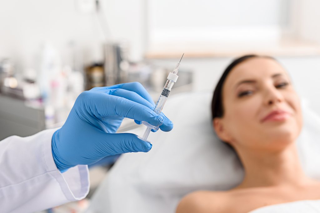 Doctor hand holding medical syringe while patient smiles in background