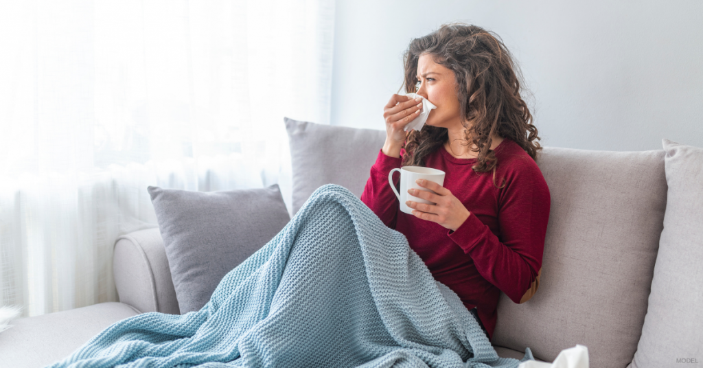 Woman with a cold sitting on couch blowing nose and drinking tea