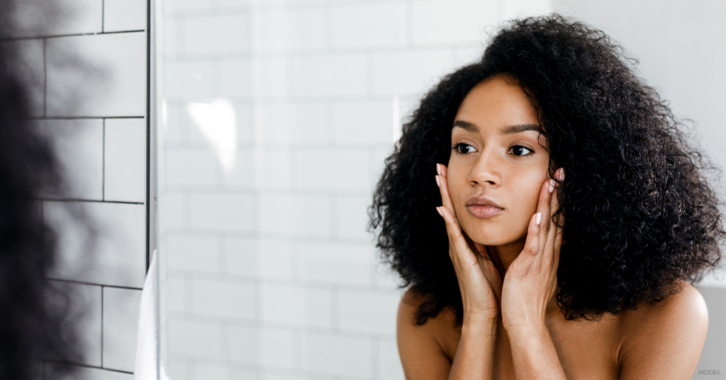 Woman in bathroom examining her face in the mirror (model)