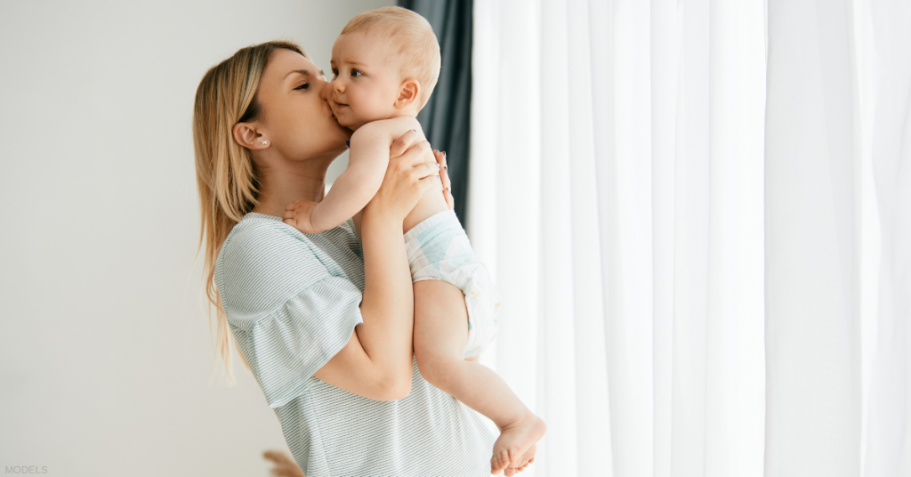 Mother holding a baby and kissing the babies cheek (models)