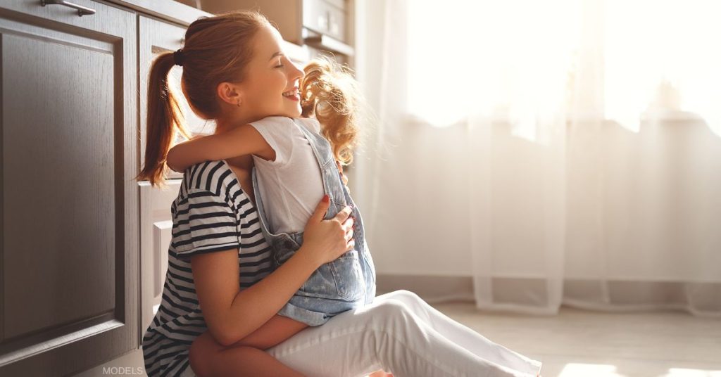 Mother sitting on kitchen floor hugging her daughter (models)